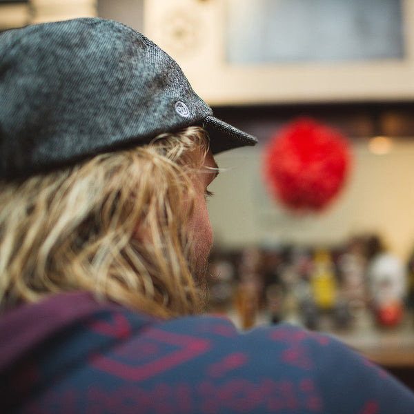 Back view of a man sitting at a bar wearing the black tweed wool velo/city cap.