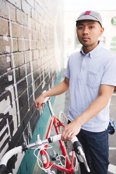Man with bike wearing cardinal herringbone cap.
